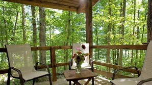 A wooden deck with two chairs and a table, surrounded by a wooden railing, overlooking a forested area. - Montfair Resort Farm (Crozet)