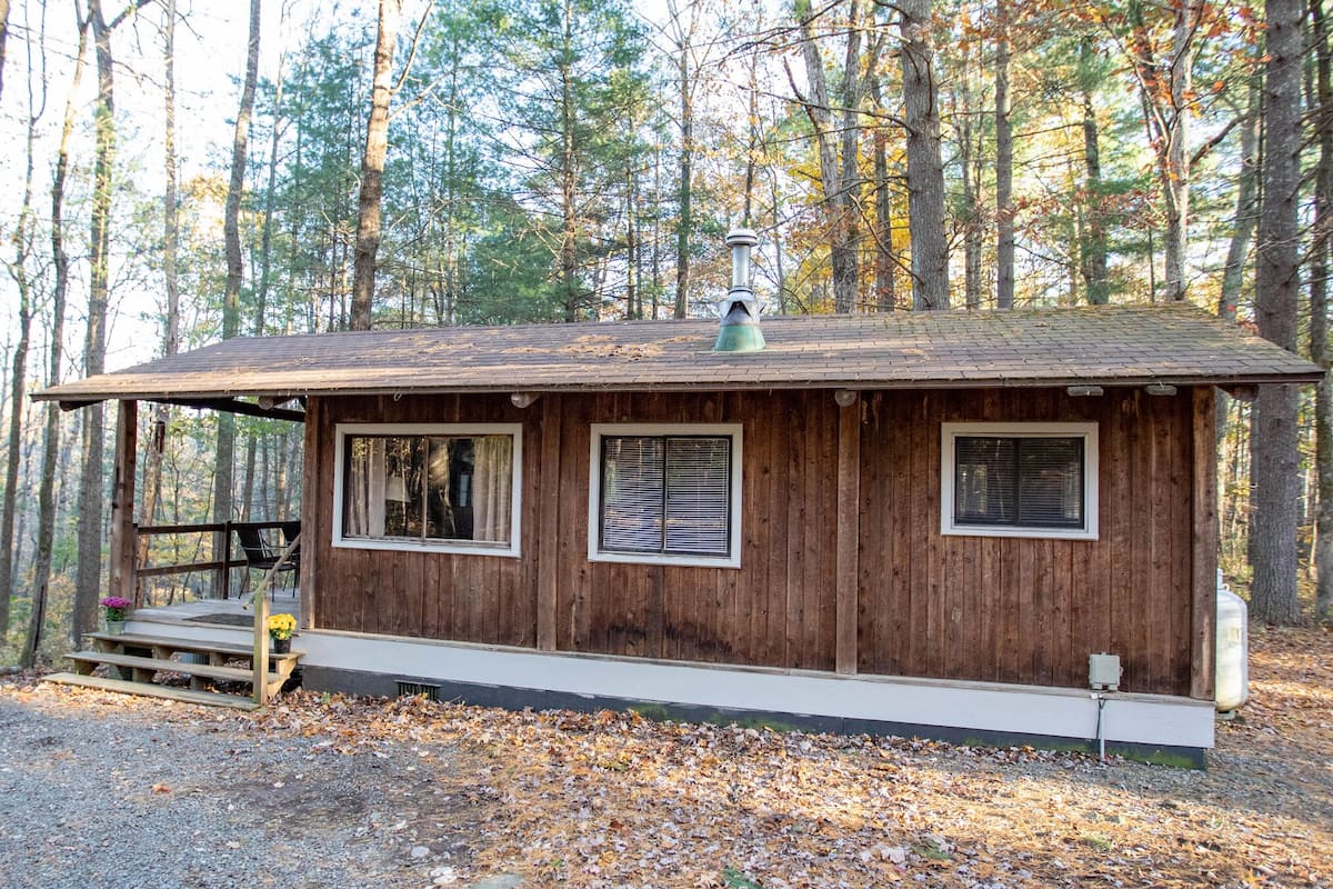 A wooden cabin with a porch, two windows, and a chimney.