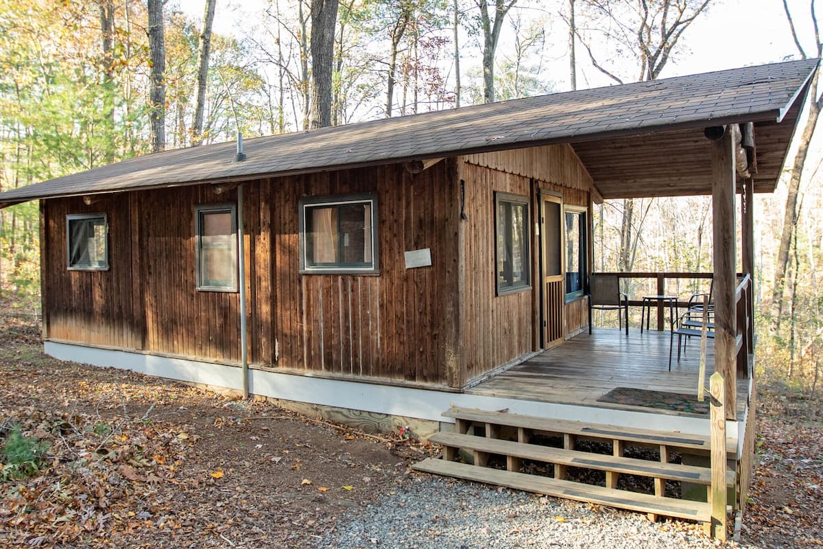 A wooden cabin with a porch, windows, and a small outdoor seating area.
