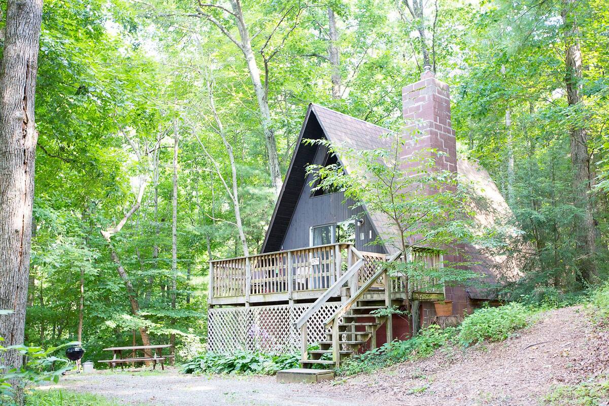 A cabin with a wooden deck and a chimney, surrounded by trees.