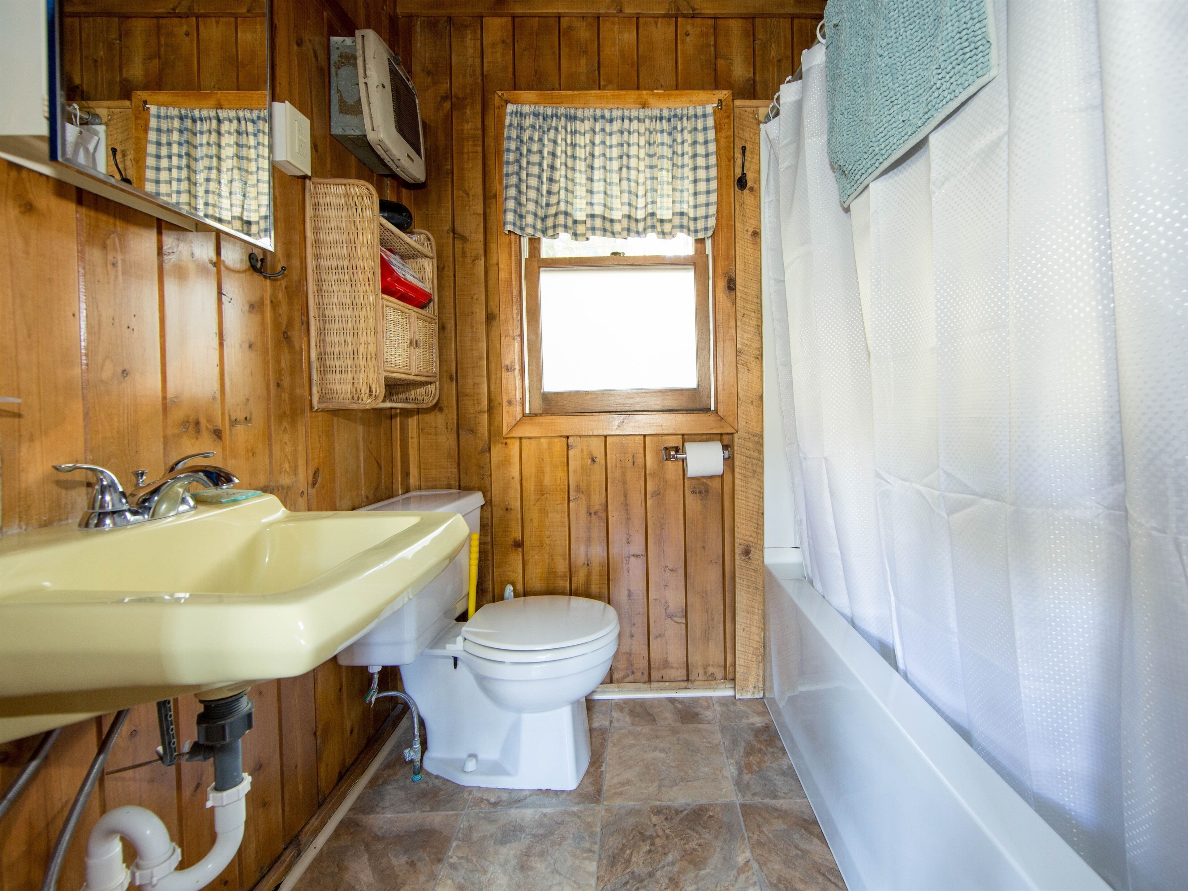 A wooden-paneled bathroom with a sink, toilet, and window.