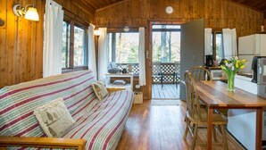 A cozy cabin interior with a wooden floor, a striped sofa, a dining table with chairs, and a kitchen area visible through an open door. - Montfair Resort Farm (Crozet)