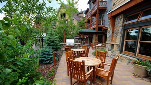 An outdoor patio area with wooden tables and chairs, surrounded by lush greenery and a stone wall. - Black Bear 8035 by SummitCove Vacation Lodging (Keystone)