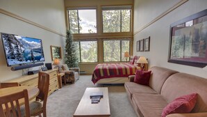 A cozy living room with a large TV, a bed, a coffee table, and a fireplace. - Slopeside 2771 (Keystone)