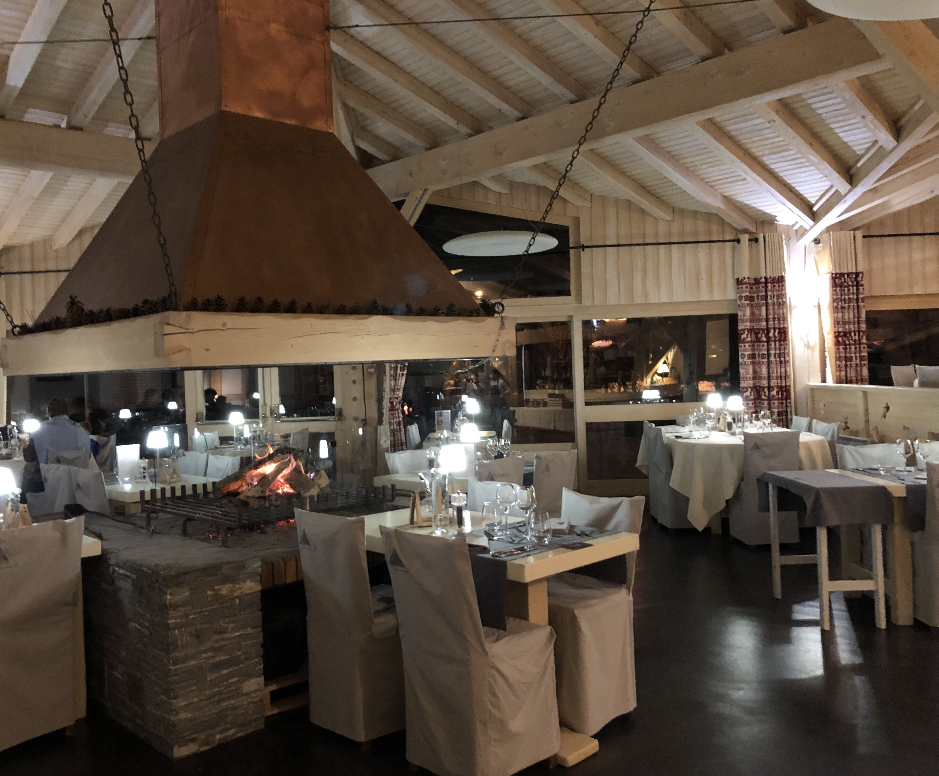 Un restaurante con mesas dispuestas para comer, una chimenea grande en el centro y vistas al exterior a través de ventanas.