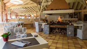Een restaurant met een grote stenen open haard, houten balken en gedekte tafels.