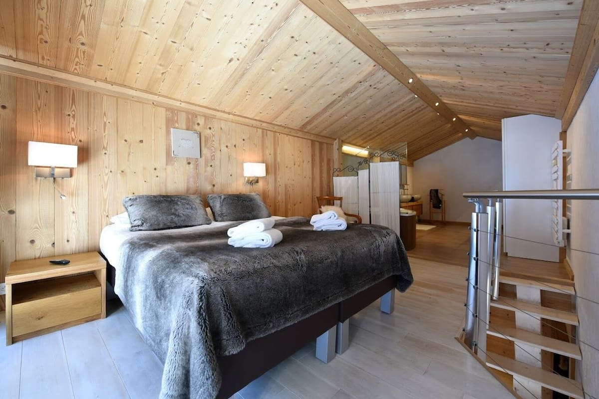 Ein Schlafzimmer mit Holzwandverkleidung, einem Bett, Nachttischen und einer Treppe.