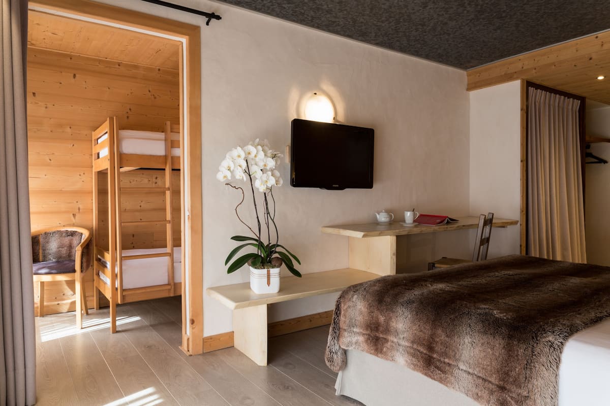 Ein modernes Hotelzimmer mit einem Holzstockbett, einem flachbildfernseher an der Wand, einem kleinen Schreibtisch mit einer Tasse und einer roten Ordner sowie einer Bank mit einer Topforchidee.