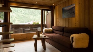 Een gezellige kamer met houten details, een bruine bank, een zachte witte plaid en een tafel met een waterkoker en glazen.