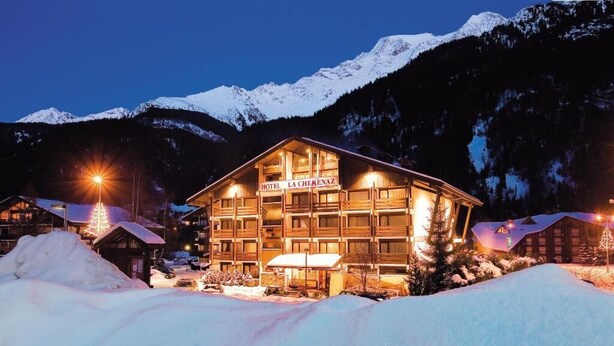 Een hotel met een bord waarop 'HOTEL LA CHEMENAZ' staat, gelegen in een bergachtig gebied met besneeuwde omgeving.