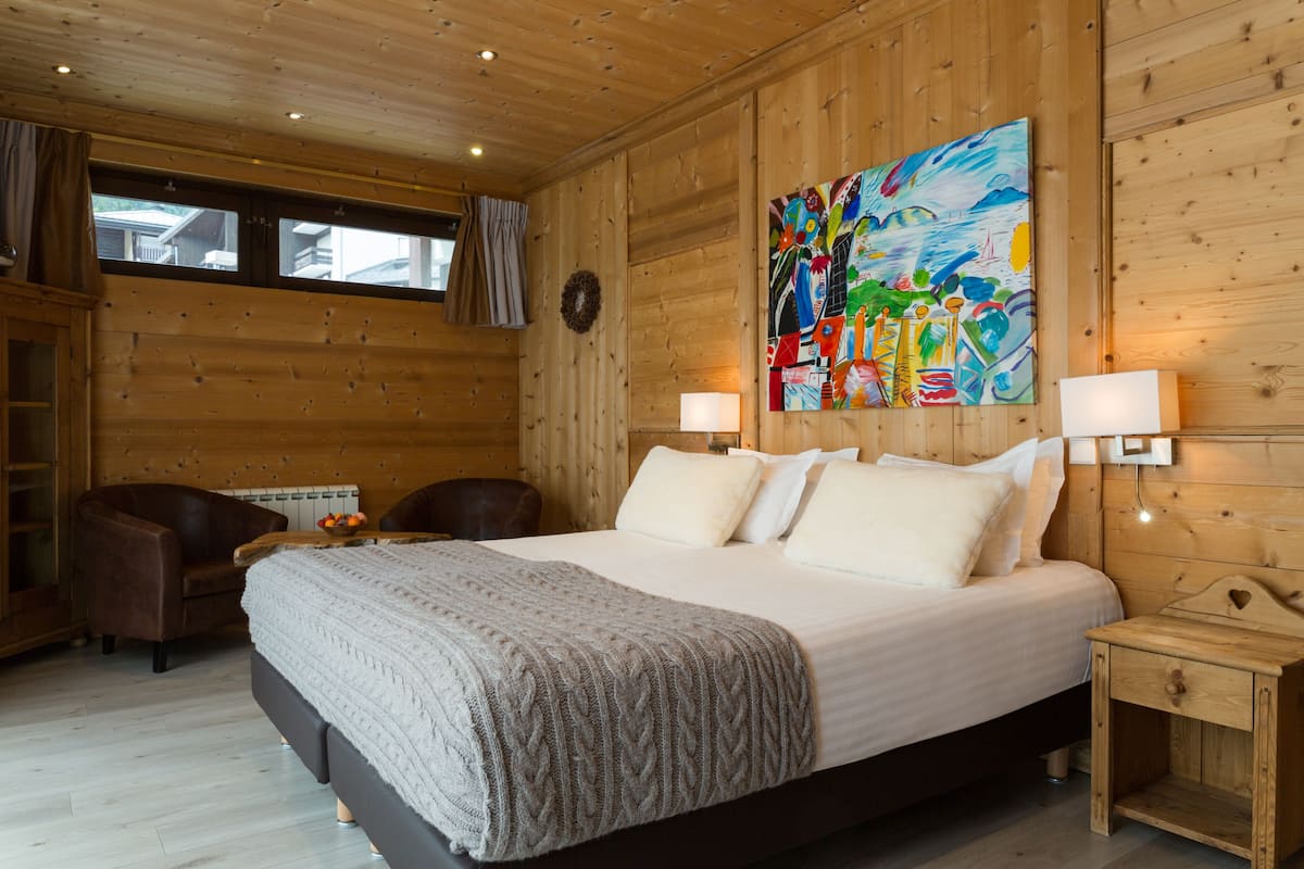 Ein Schlafzimmer mit Holzvertäfelung, einem großen Bett, zwei Nachttischlampen, einem Sessel und einem Bild an der Wand.