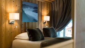 Een gezellige kamer met een bed, twee wandlampen, een schilderij van een berglandschap en een raam met gordijnen.