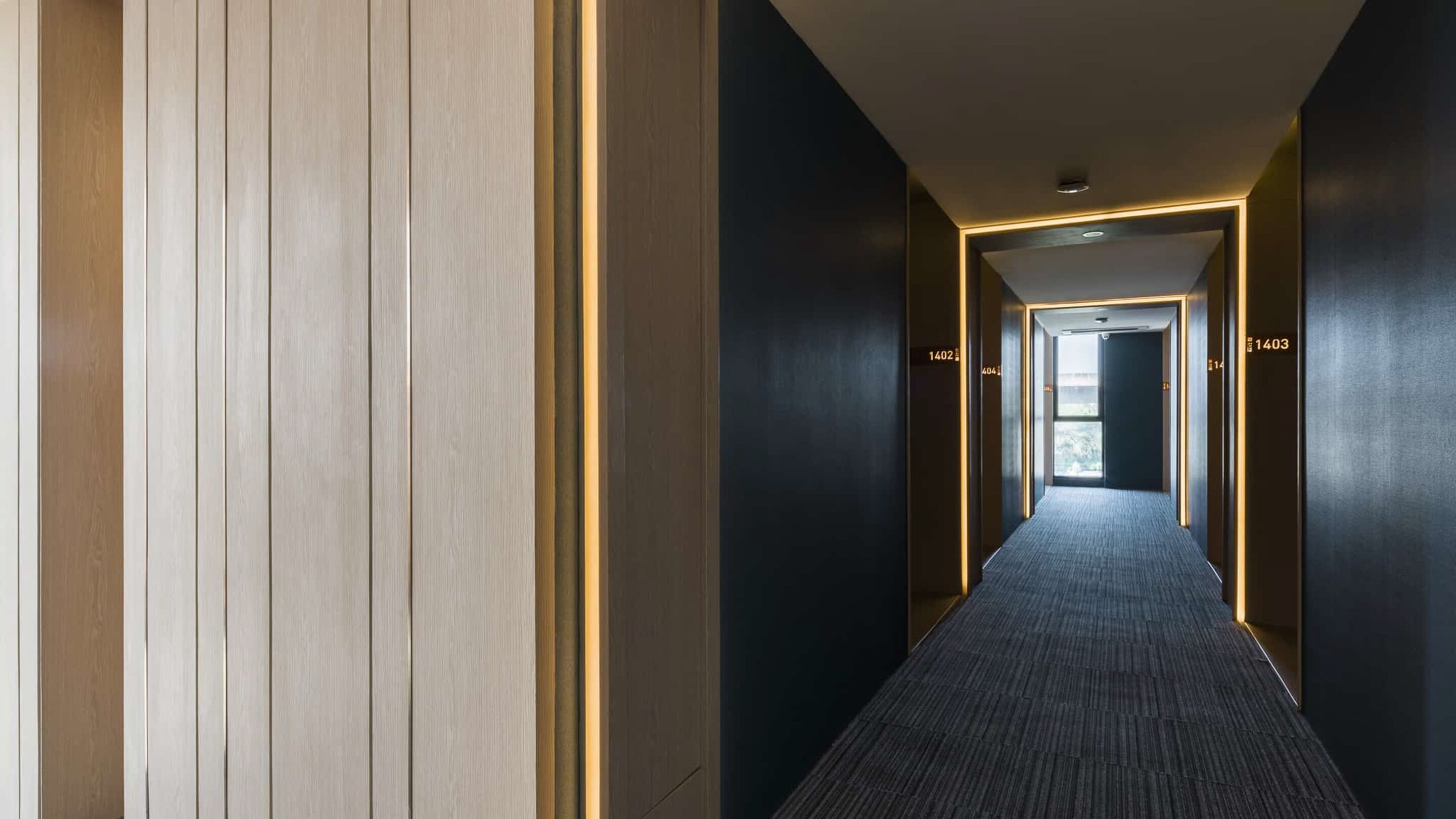 A modern hotel corridor with a carpeted floor, wooden panel walls, and illuminated doorways numbered 1402 and 1403.