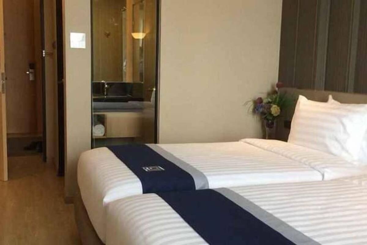 Een hotelkamer met twee bedden, een badkamer met een spiegel en een kleine tafel met een bloemenvaas.