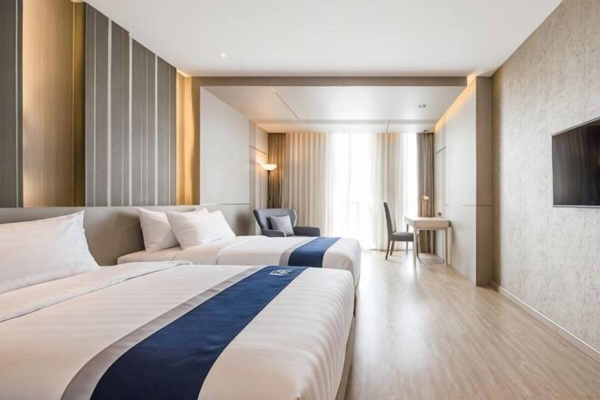 Een hotelkamer met twee bedden, een bureau, een stoel en een groot raam.
