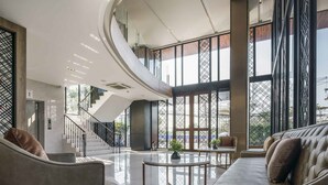 Een ruime lobby met een gebogen plafond, een trap en een zithoek met een bijzettafeltje.
