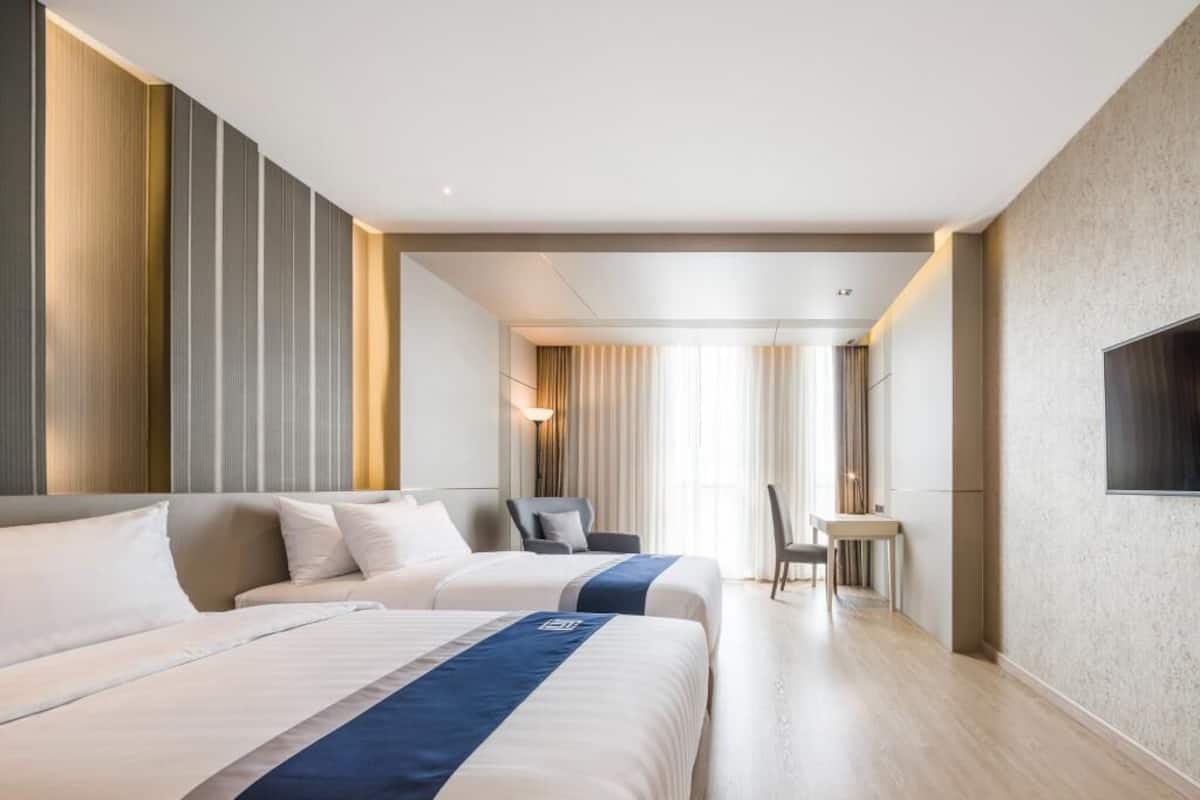 Een hotelkamer met twee bedden, een bureau, een stoel en een aan de muur bevestigde televisie.