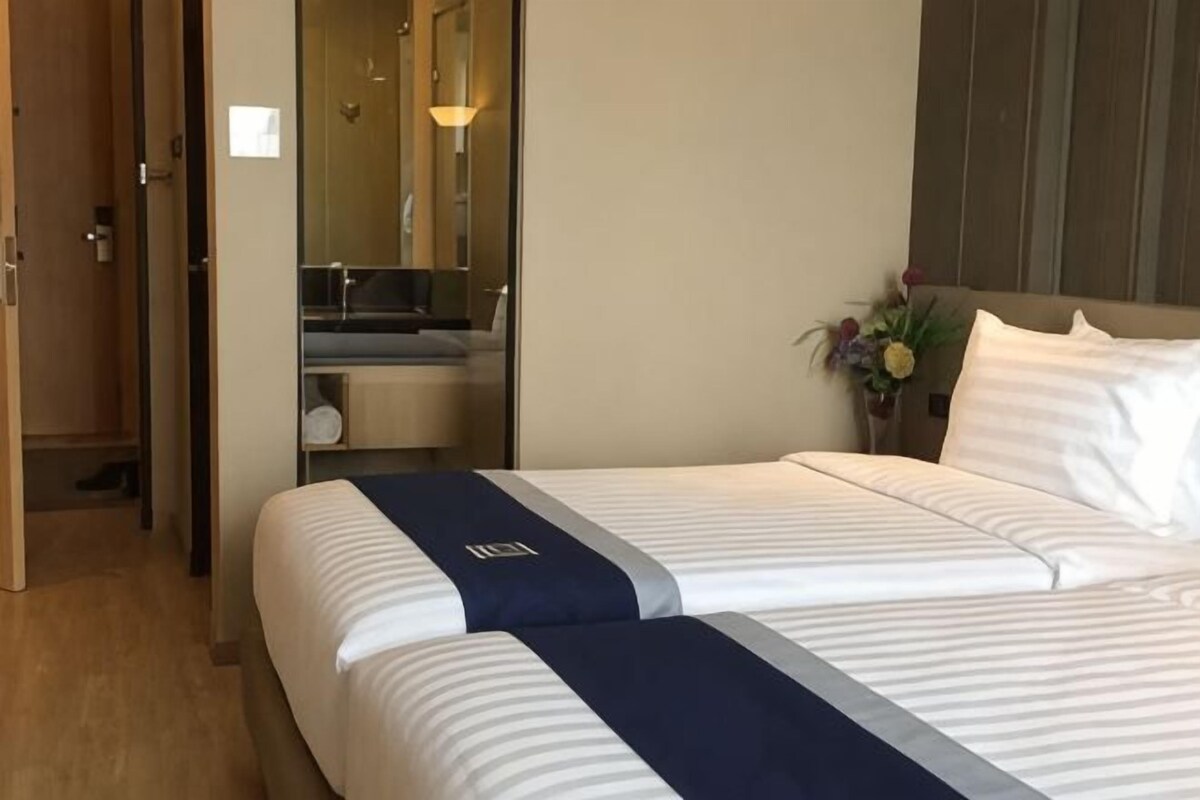 Een hotelkamer met twee bedden, een badkamer met spiegel en een kleine plant op het nachtkastje.