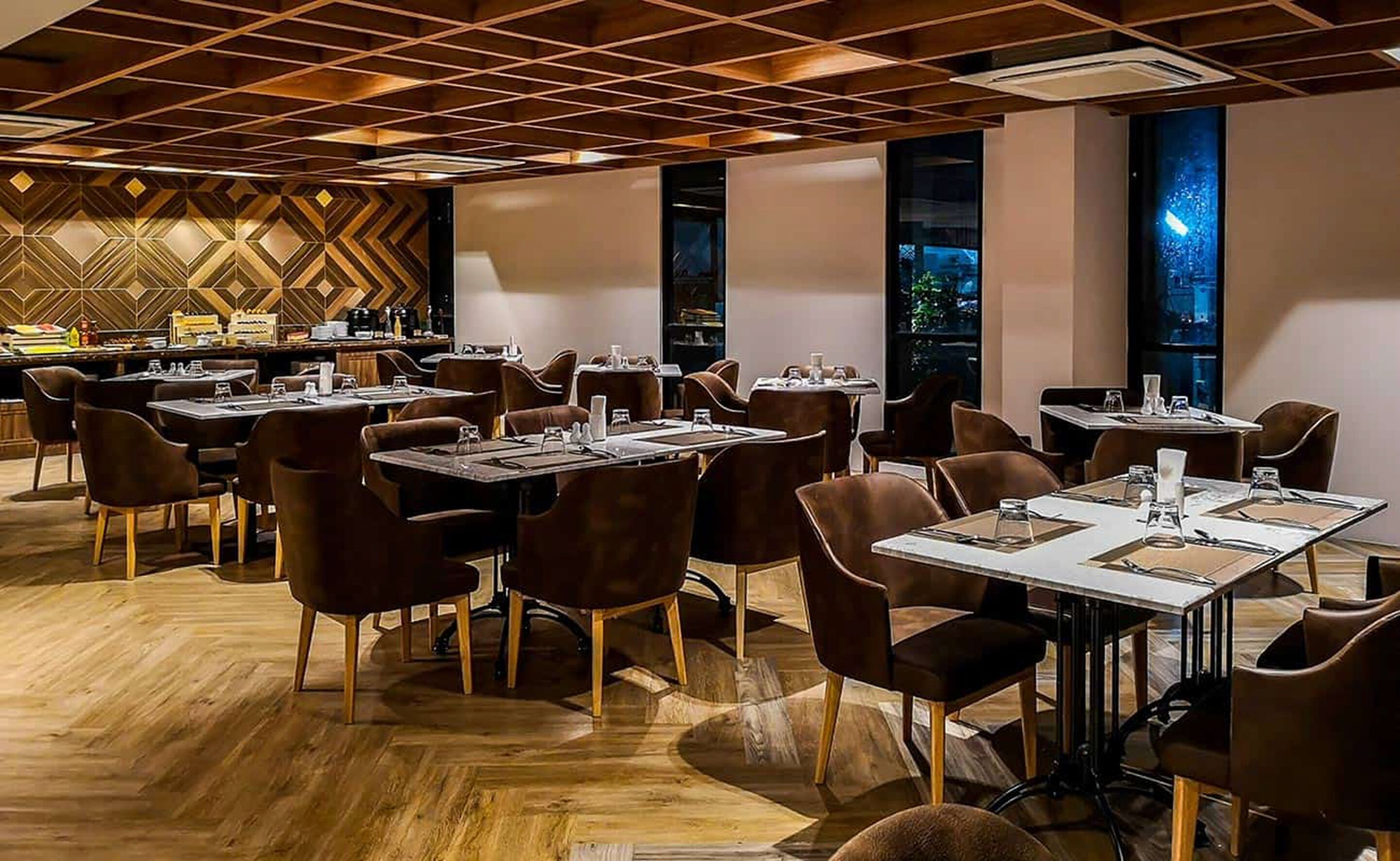 Un espace de restauration moderne, doté de plusieurs tables et chaises, d’un mur orné de motifs et d’un plancher en bois.