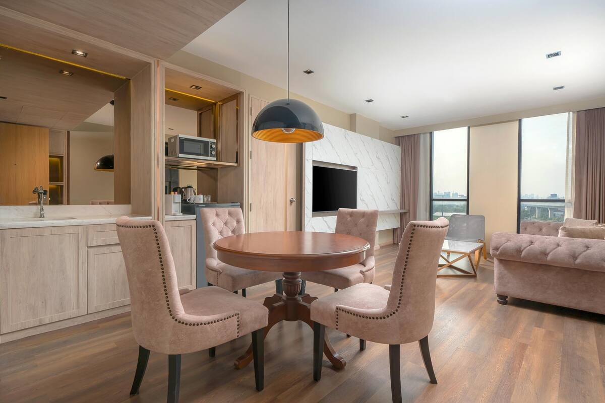Een moderne woonkamer met een ronde houten tafel, vier gestoffeerde stoelen, een flatscreen-tv en grote ramen met uitzicht op de stad.