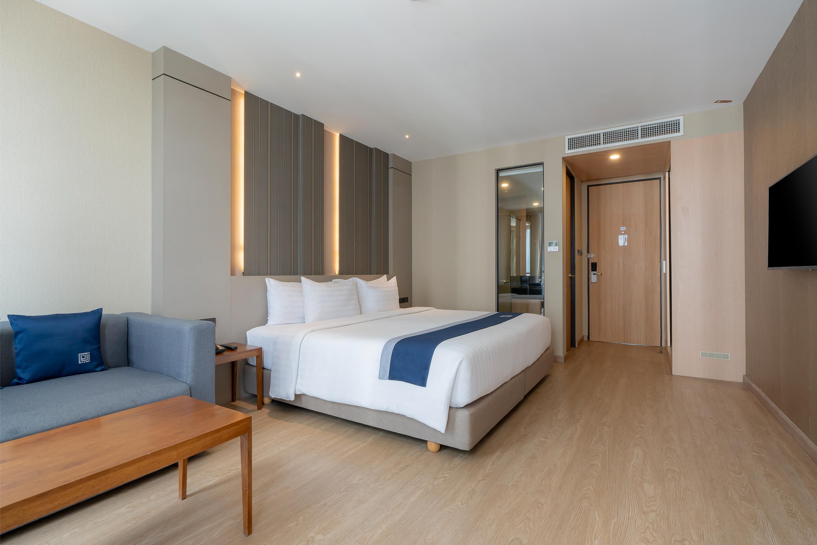 A hotel room with a bed, a sofa, a wooden table, and a TV mounted on the wall.
