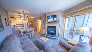 En moderne stue med pejs, grå sofaer og et spiseområde med en lysekrone.