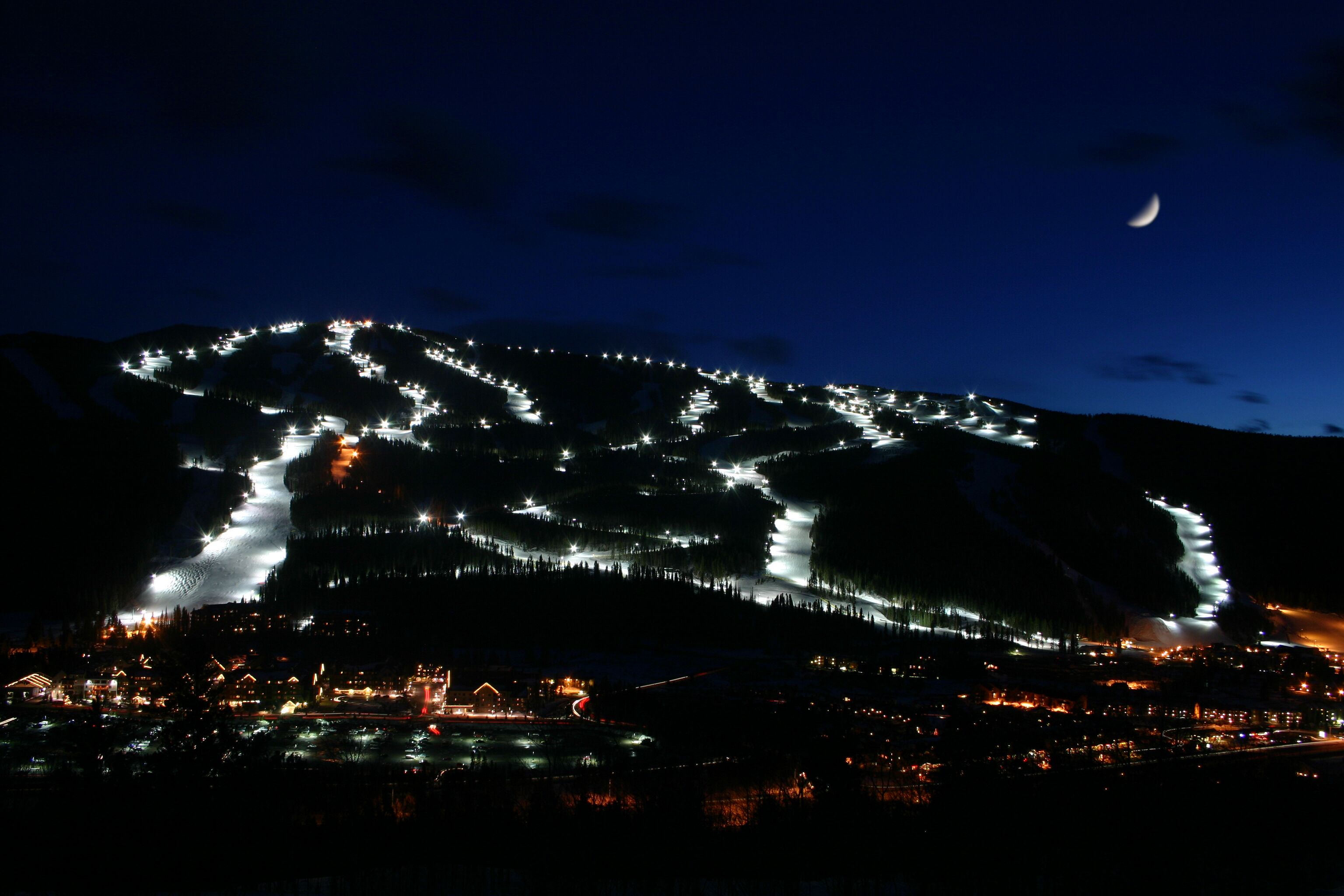 A nighttime view of a mountain with a winding road and a small settlement at its base.