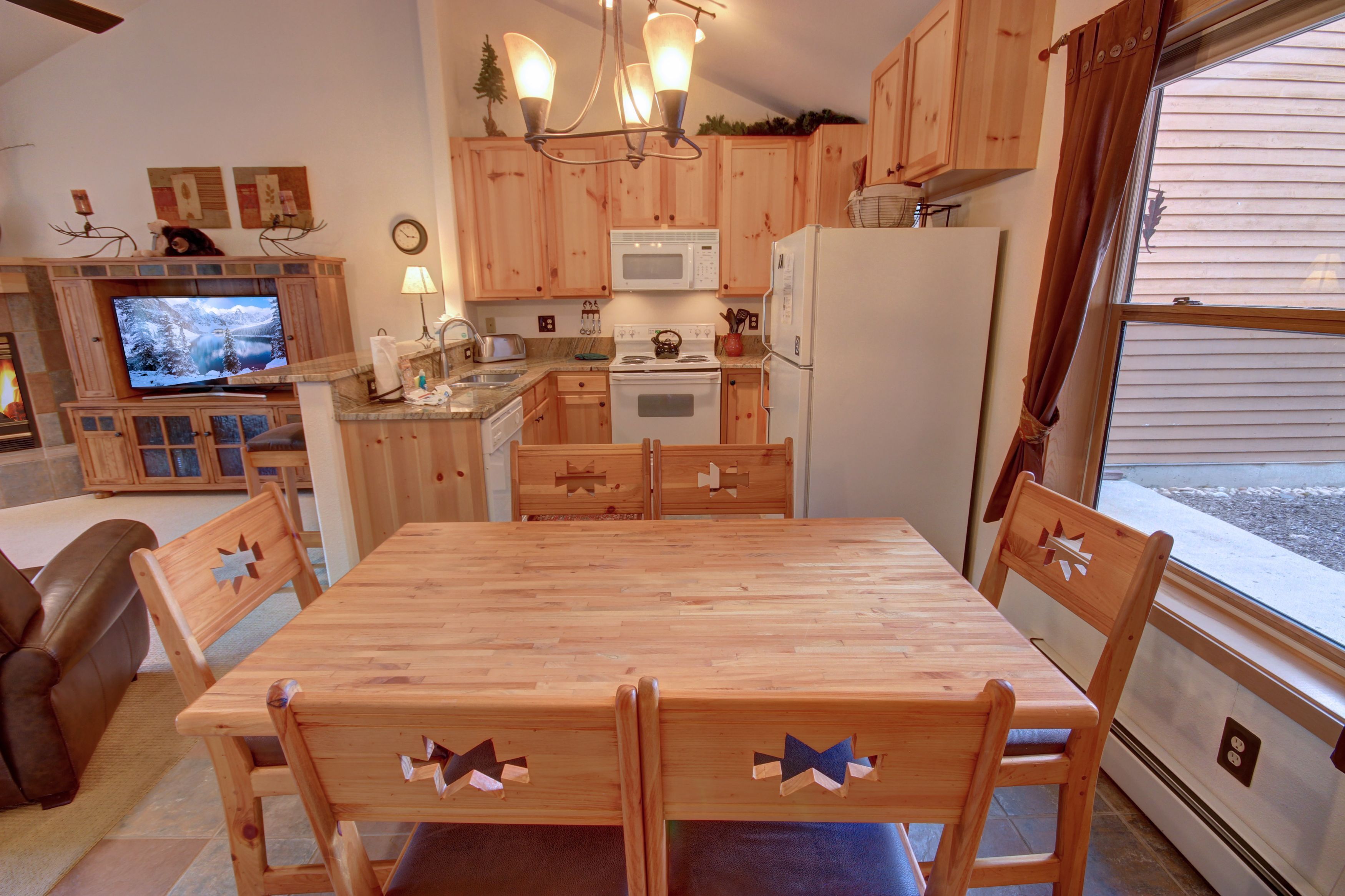 Ett kompakt kök med träskåp, en mikrovågsugn, ett kylskåp och ett matbord med stolar.