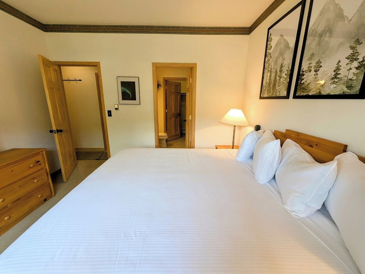 A bedroom with a large bed, wooden dresser, and a door leading to another room.
