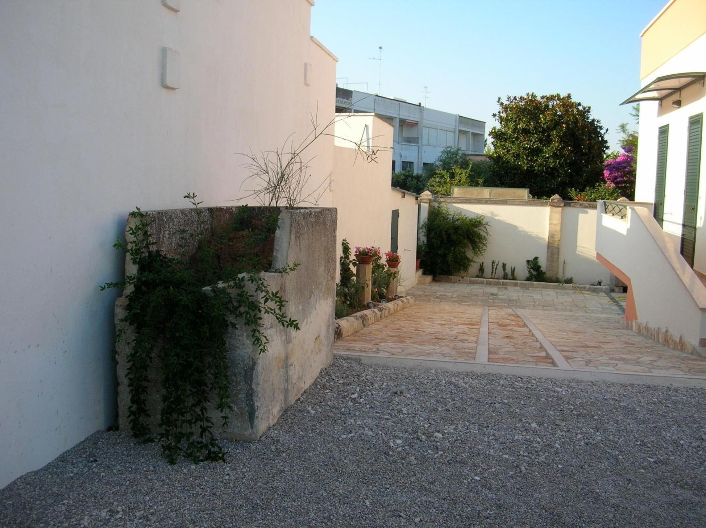 Un patio con un camino de grava, una jardinera de hormigón con plantas y un edificio con balcón.