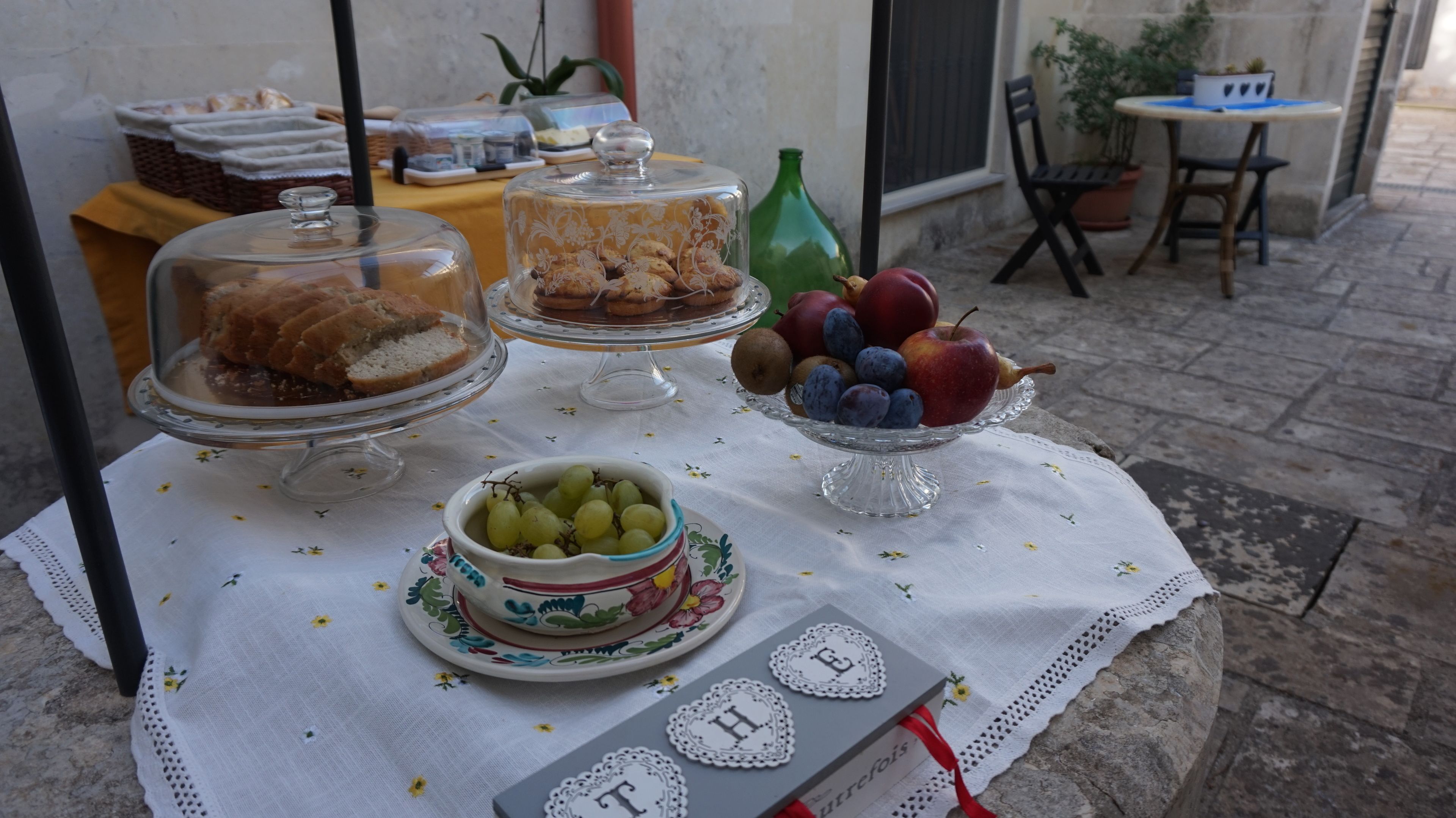 A table with covered food items, a bowl of grapes, and a fruit bowl with apples and blueberries.