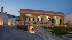 A modern building with a central patio area, outdoor seating, and a well-lit entrance. - Casina dei Nonni (Carpignano Salentino)