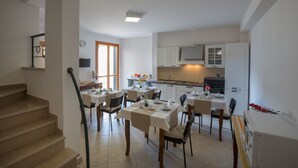 A dining area with tables set for four, a kitchen with white cabinets, and a staircase leading to another level. - Casina dei Nonni (Carpignano Salentino)