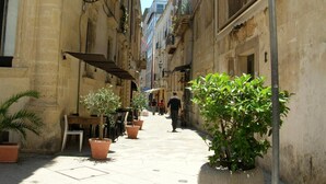 A narrow street with buildings on either side, outdoor seating, and a pedestrian sign. - Casina dei Nonni (Carpignano Salentino)