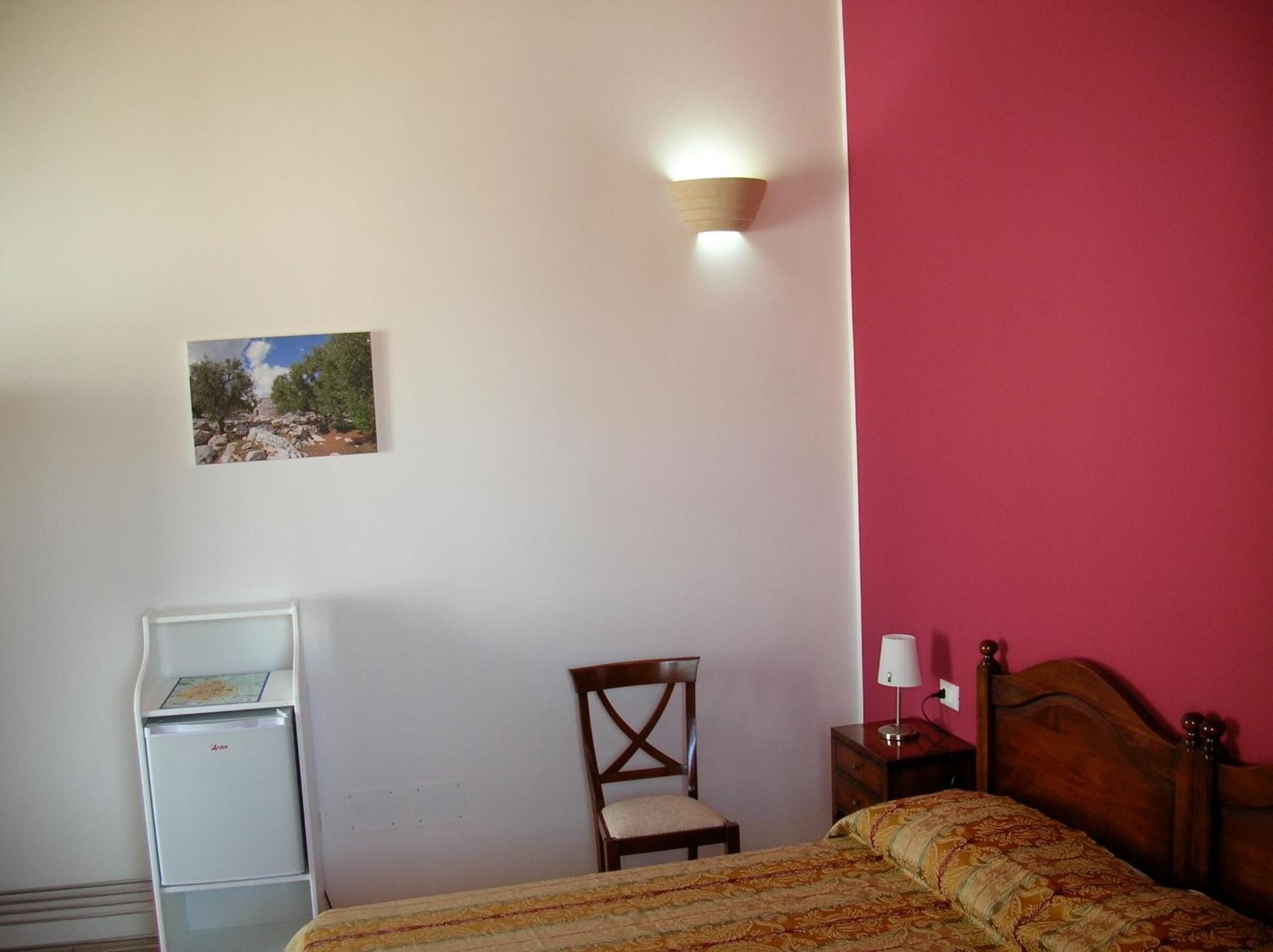 Un dormitorio con cama, una silla, un escritorio y una lámpara de pared.