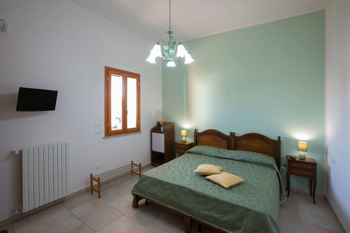 Une chambre à coucher avec un lit, des lampes de chevet, un radiateur, une télévision et une fenêtre.