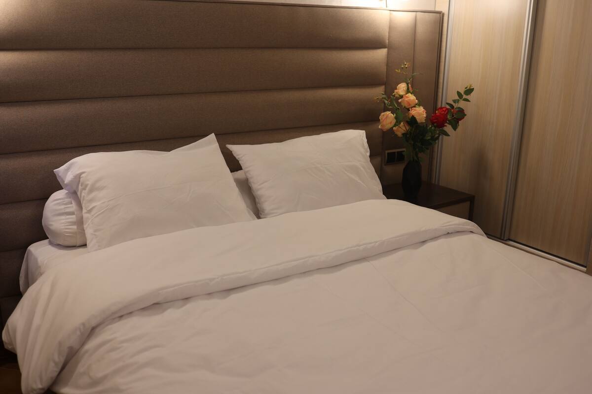 A neatly made bed with white linens and a headboard.