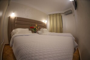 A hotel room with two beds, a headboard, a wall-mounted air conditioner, and a curtain. - Hôtel Des Lilas (Oujda)