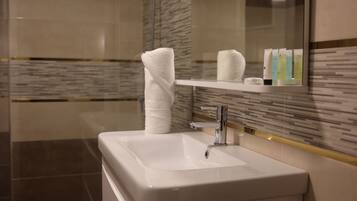 Un baño con lavamanos blanco, una toalla y artículos de aseo en un estante.