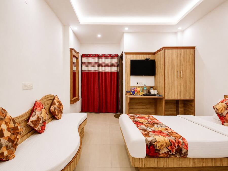 A hotel room with two beds, a desk with a TV, a wardrobe, and a bathroom with a red curtain.