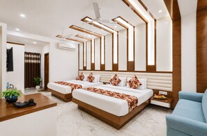 A modern hotel room with two beds, a blue armchair, a wooden floor, and a ceiling fan. - New Hindustan By Backpackers Heaven (New Delhi)