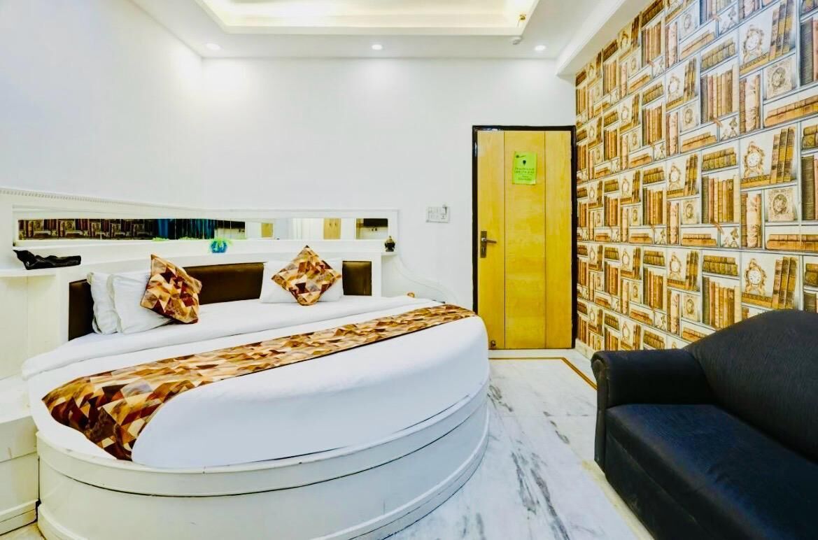 Ein modernes Hotelzimmer mit einem bogenförmigen Bett, einer schwarzen Couch, einer strukturierten Wand und einer Holztür.