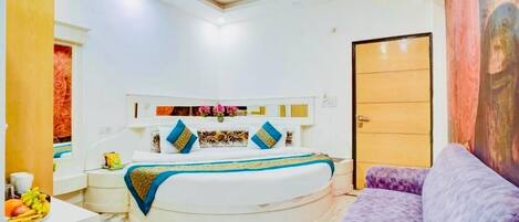A bedroom with a bed, a nightstand, a purple sofa, a ceiling fan, and a door.