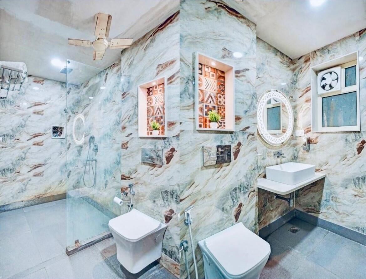 Un bagno con pareti in marmo, due servizi igienici, un lavandino, una ventola a soffitto e pannelli decorativi.