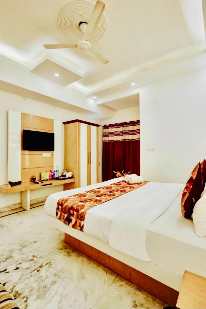 Habitación de hotel con cama, ventilador de techo, televisor, armario y escritorio con espejo.