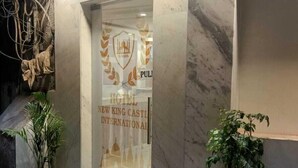 Entrada de hotel con fachada de mármol, puerta de cristal y plantas en macetas en la acera.