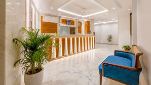 Un área de recepción con suelo de mármol, mostrador de recepción, una silla azul y plantas en macetas.