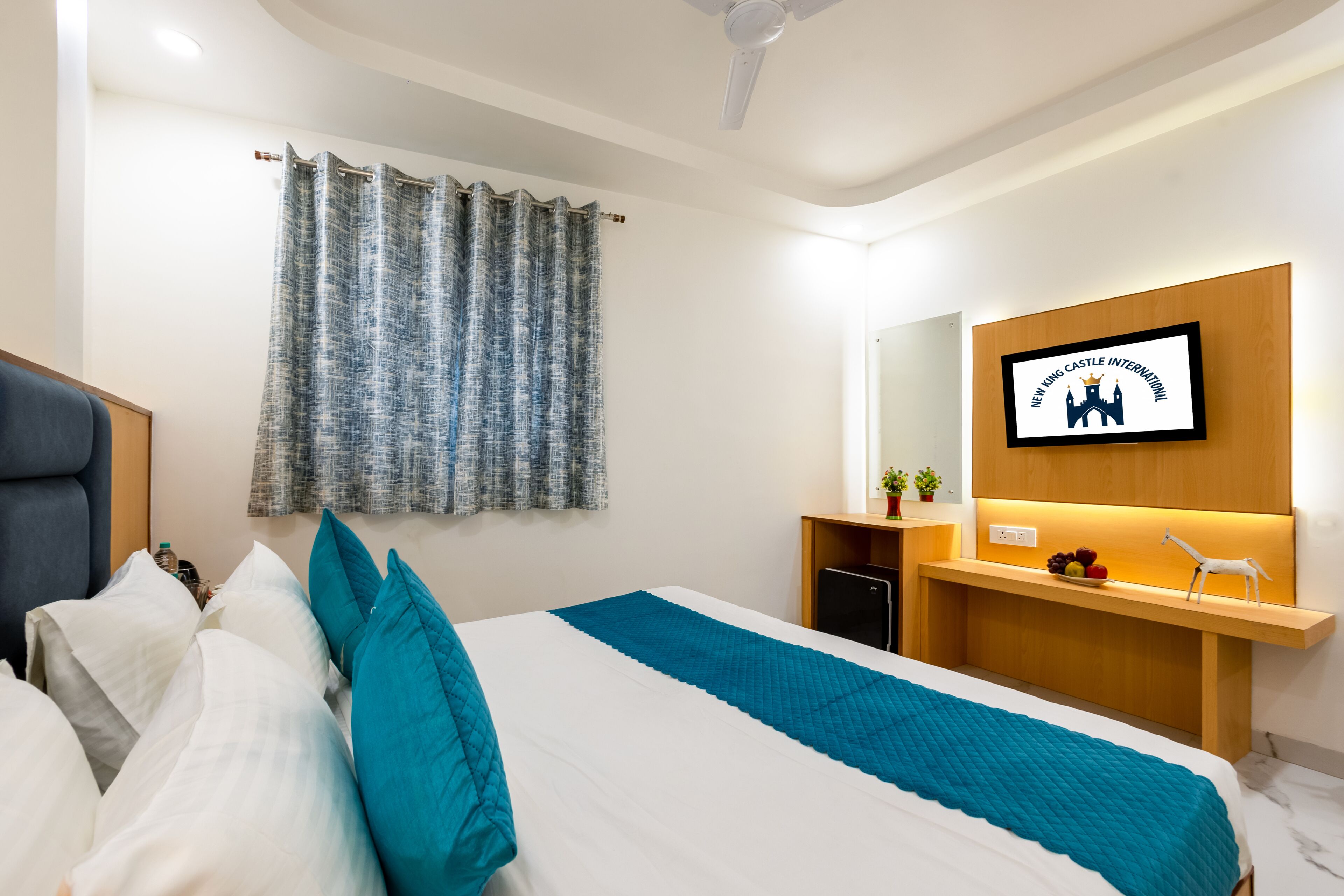 Een moderne hotelkamer met een bed, een bureau, een televisie en een wandplank met een fruitschaal en een klein beeldje.