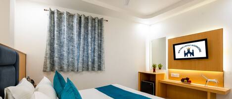 Een moderne hotelkamer met een bed, een bureau, een televisie en een wandplank met een fruitschaal en een klein beeldje.