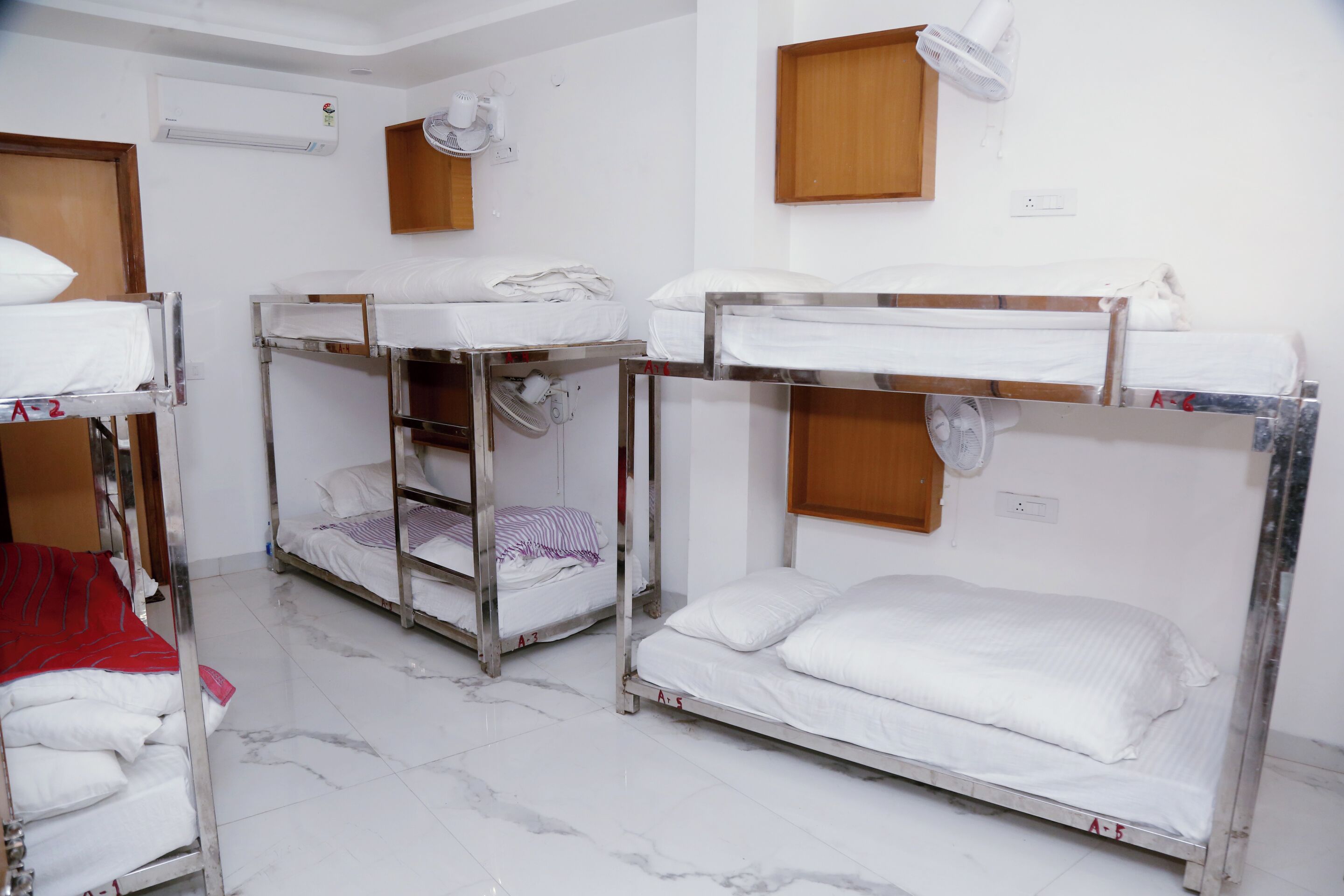 Ein Schlafsaalzimmer mit Etagenbetten, einem Ventilator, einer Klimaanlage und einem Holzschrank.